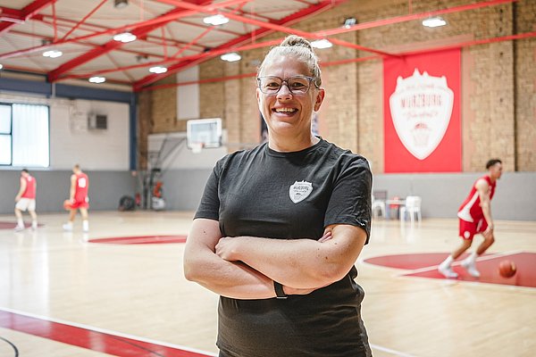 Die neue Physiotherapeutin Sabrina Damrich steht lächelnd in der Traingshalle der Fitness First Würzburg Baskets. 
